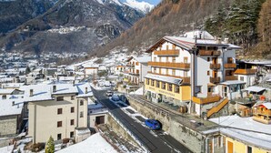 A hotel with a mountain view, a road with cars, and snow-covered buildings. - Hotel Biancospino (Lanzada)