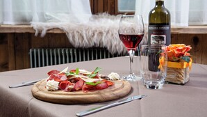 A dining table with a wooden board of food, a wine glass, a bottle of wine, and a vase with flowers. - Hotel Biancospino (Lanzada)