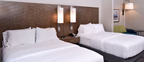 A hotel room with two beds, a wooden headboard, bedside lamps, a nightstand, and a small table with a lamp.