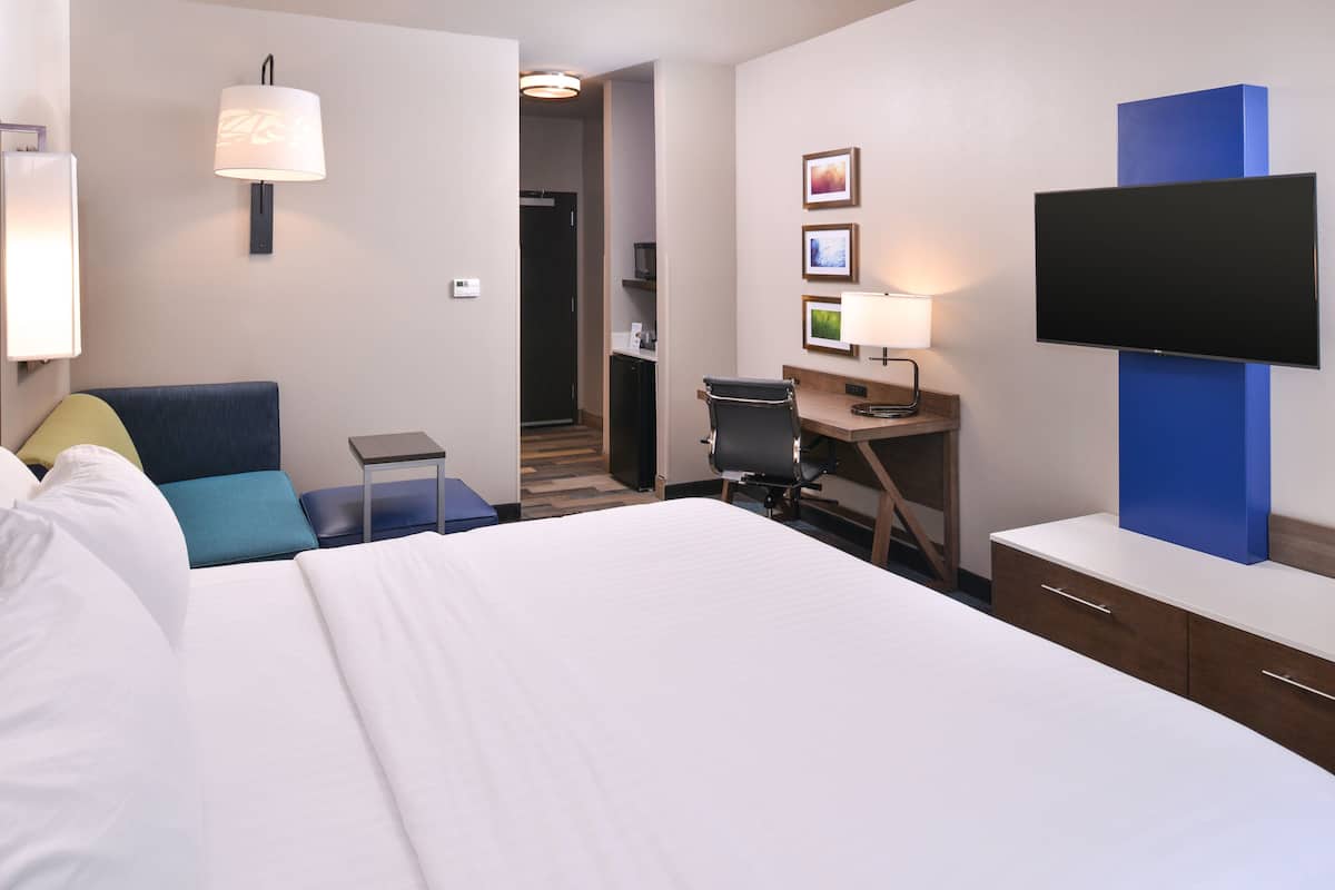 Habitación de hotel con cama, escritorio, silla, televisor y una pequeña kitchenette.