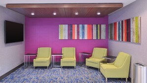 A room with a purple wall, three yellow chairs, a TV, and colorful artwork. - Holiday Inn Express & Suites Bryant - Benton Area by IHG (Benton)