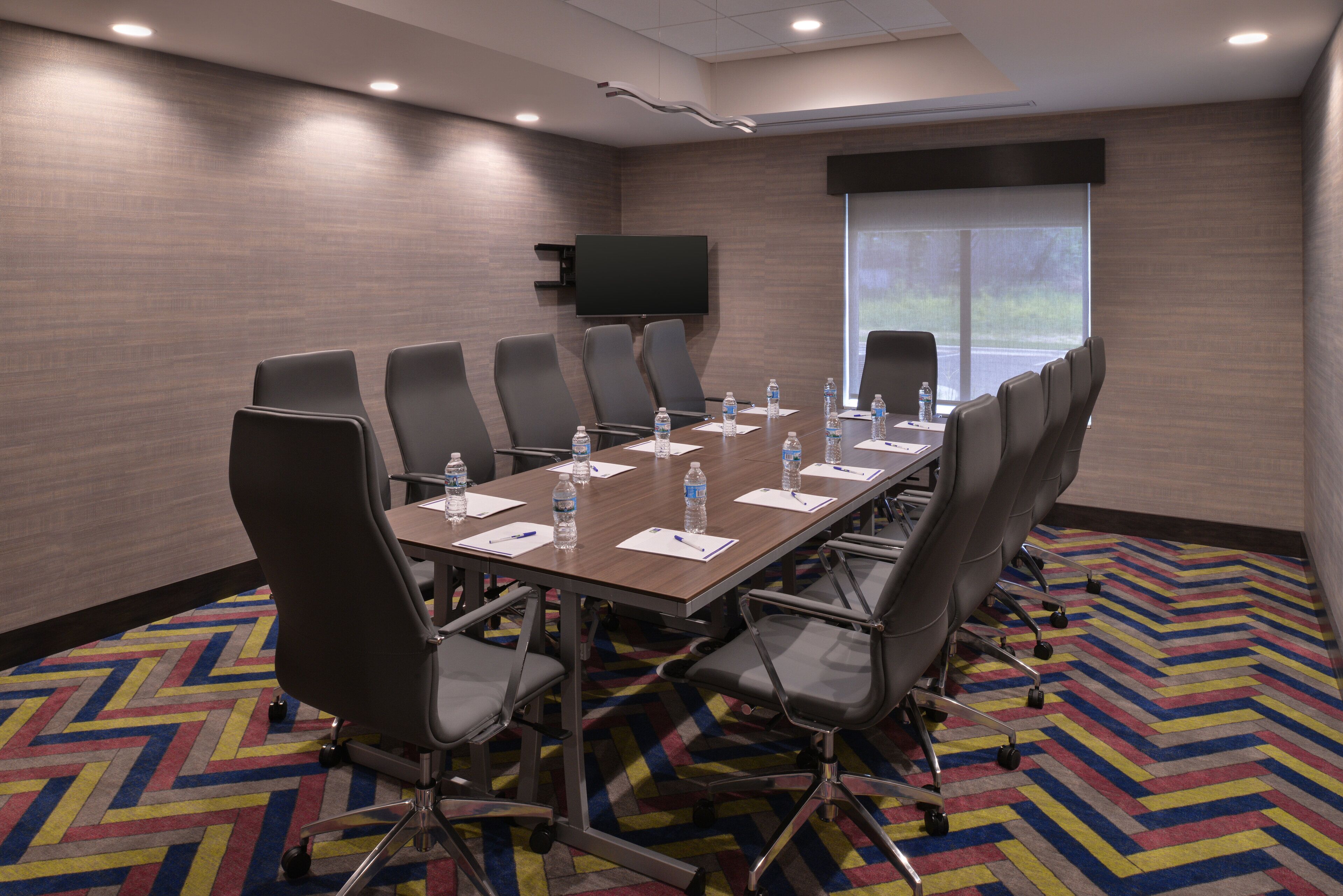 A conference room with a large table, chairs, water bottles, and a TV on the wall.