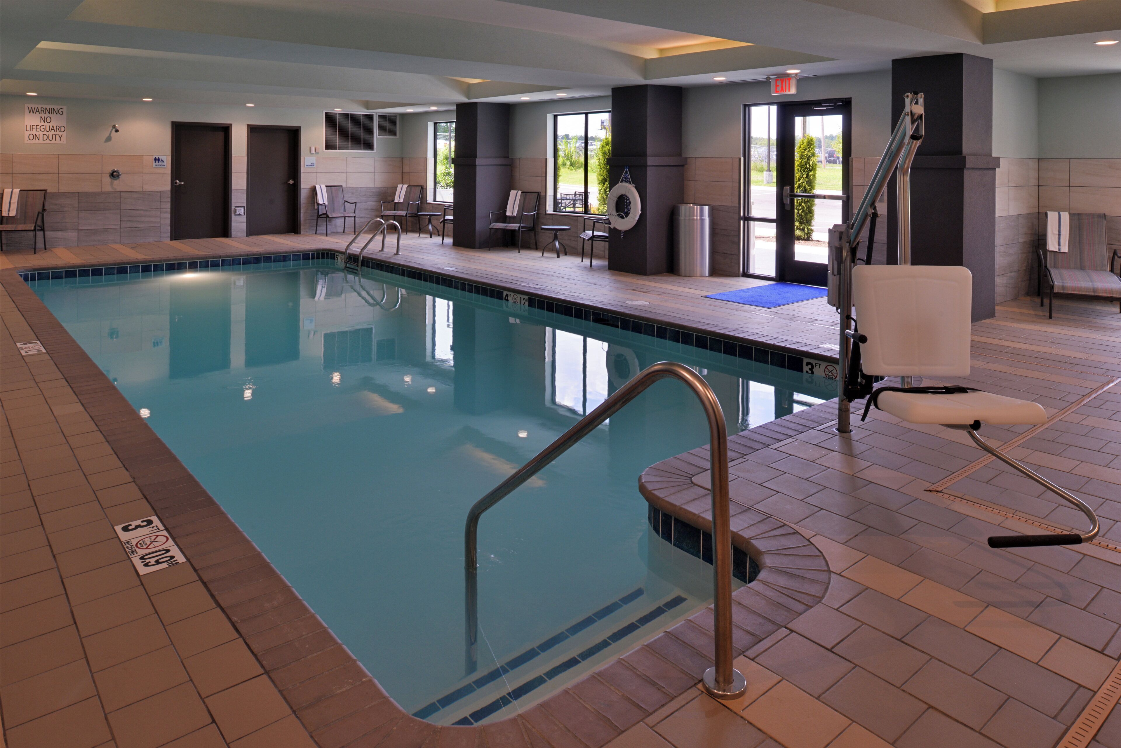 An indoor swimming pool with a lifeguard chair, a lifebuoy, and a sign indicating no lifeguard on duty.