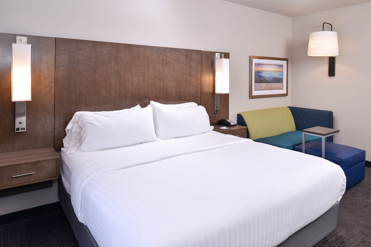 Habitación de hotel con una cama grande, una mesita de noche, un escritorio, una silla y una lámpara de pared.