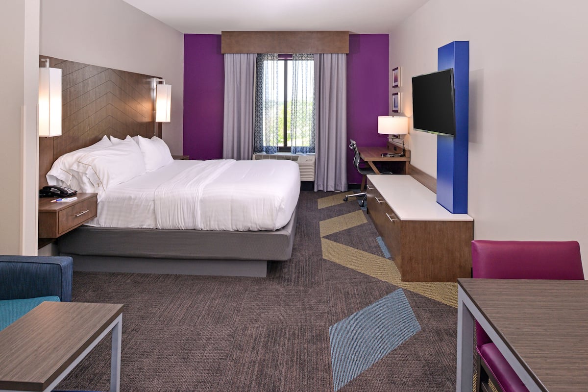 Habitación de hotel con cama, escritorio, silla, televisión y ventana con cortinas.