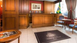 A hotel lobby with wooden paneling, a reception desk, a chair, a small table, and a doormat with the hotel's name. - Du Bresil (Paris)