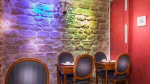 A dining area with a stone wall, wooden chairs, and a table with a tray. - Du Bresil (Paris)