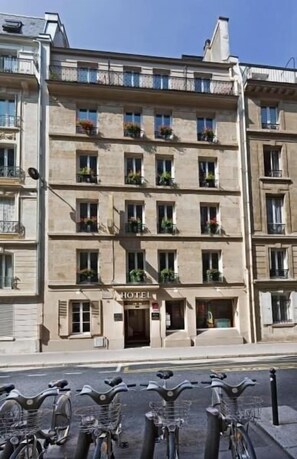 A multi-story hotel with balconies, a sign indicating it is a hotel, and a row of bicycles parked in front. - Du Bresil (Paris)