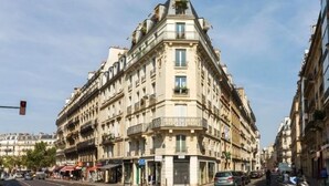 A corner building with multiple floors, balconies, and a street view with cars and pedestrians. - Du Bresil (Paris)