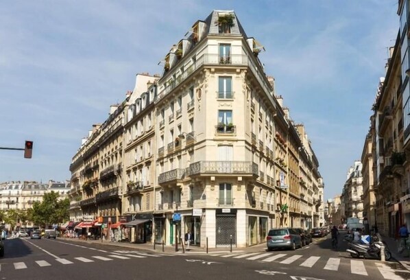 A corner building with multiple floors, balconies, and a street view with cars and pedestrians. - Du Bresil (Paris)