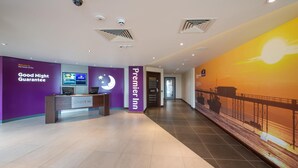 Un espace d’accueil d’hôtel avec une pancarte indiquant une « garantie de bonne nuit », une enseigne « Premier Inn » et un écran numérique affichant des informations.