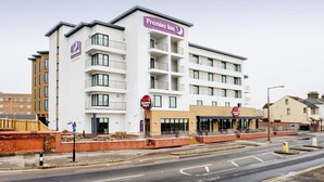 Un hôtel à plusieurs étages, reconnaissable à son grand panneau « Premier Inn », un restaurant situé au rez-de-chaussée et un mur de briques orné d’un panneau bleu.
