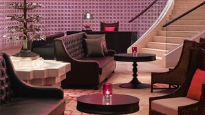 Un interior moderno con una escalera curva, una zona de estar con sofá y sillas, una mesa redonda pequeña y un árbol decorativo.