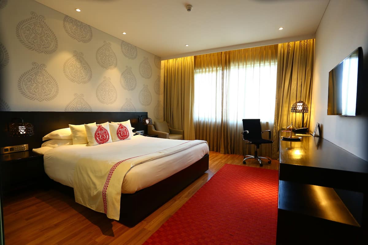 A hotel room with a large bed, a desk, a chair, a TV, and a patterned wall.