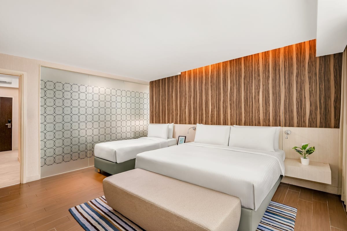 Habitació d'hotel moderna amb dos llits, una paret decorativa de fusta, un mural amb un disseny geomètric i una petita planta en test.
