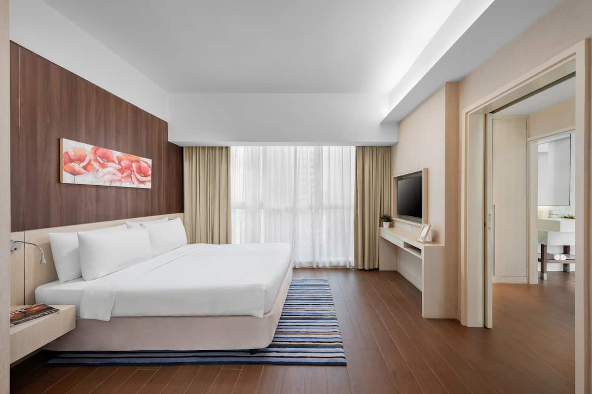 Habitació d'hotel moderna amb un llit gran, una televisió de pantalla plana, un panell de fusta al capçal i una finestra gran amb cortines lleugeres.