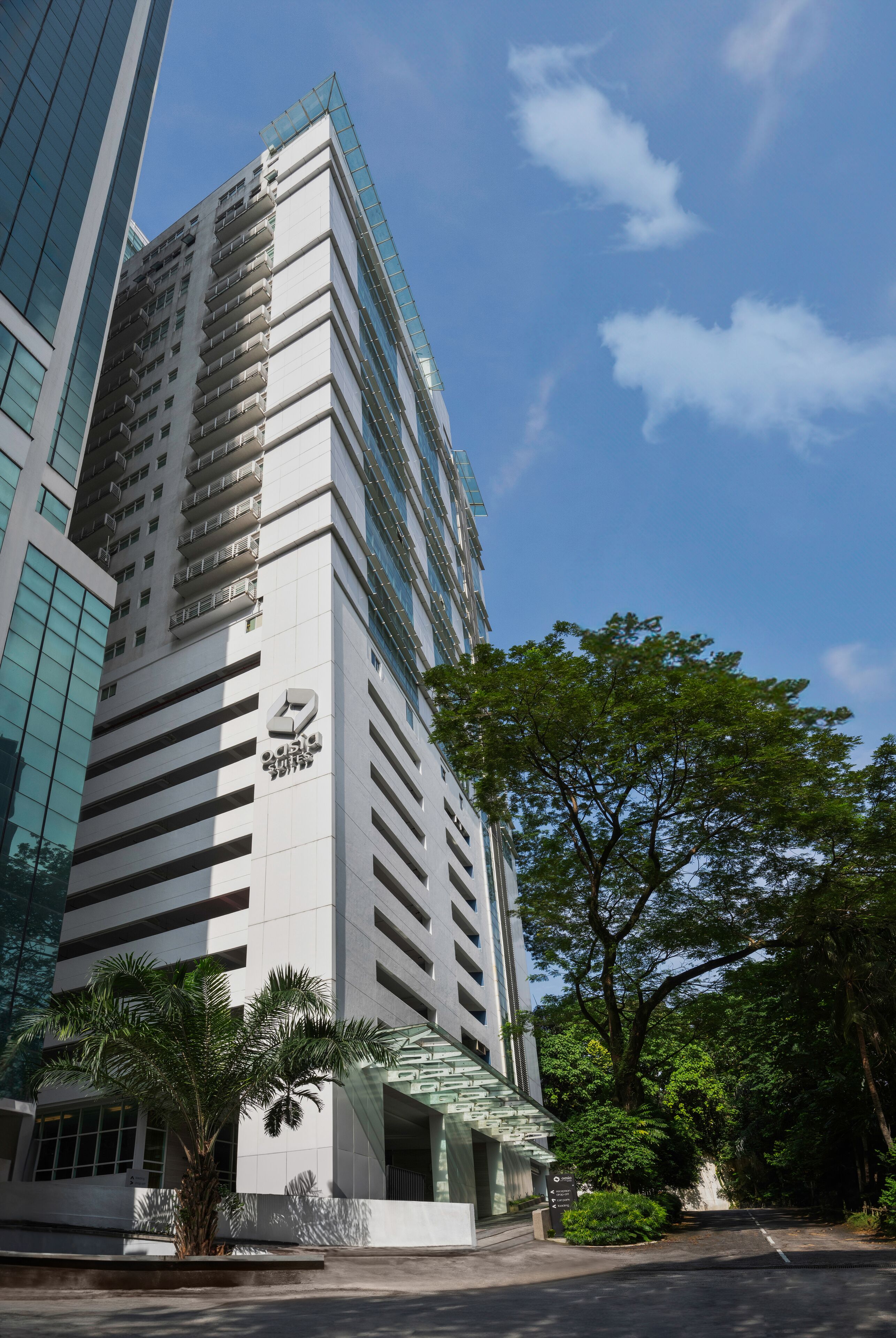 A modern high-rise building with a prominent logo on the facade, surrounded by lush greenery and a clear blue sky.