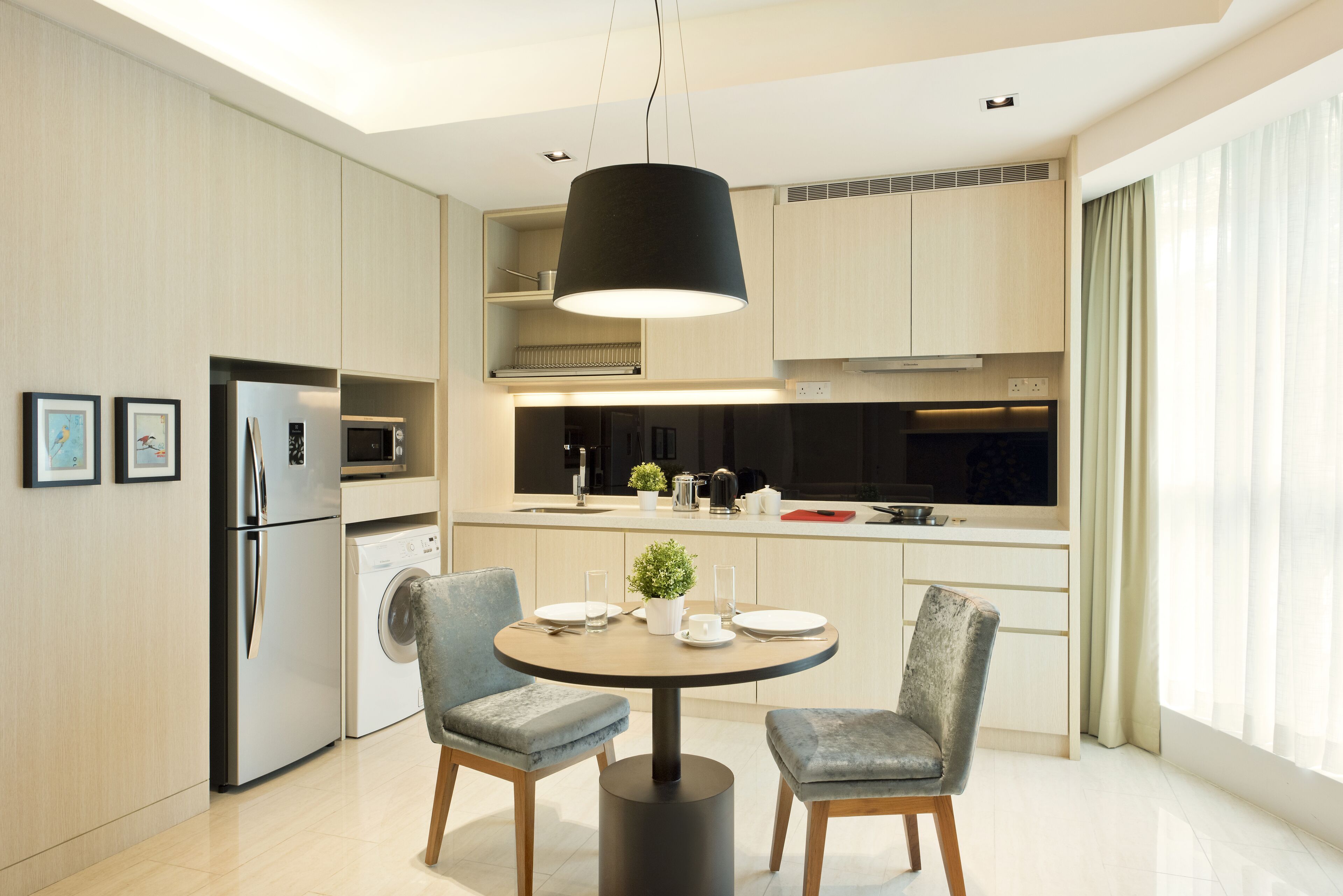 A modern kitchen with a dining area, featuring a round table, two chairs, a hanging light fixture, and built-in appliances.