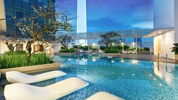 Une piscine intérieure à l’eau d’un bleu cristallin, avec des chaises longues blanches et un bâtiment moderne en arrière-plan.