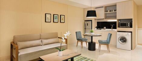 A compact living space with a sofa, a coffee table, a dining table with chairs, a kitchen area with a microwave, and a washing machine.