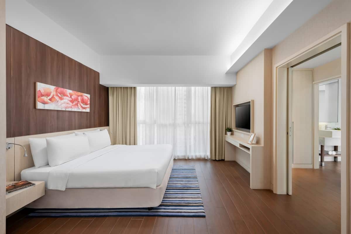 Habitació d'hotel amb un llit gran, televisió, escriptori i un bany visible a través d'una porta oberta.