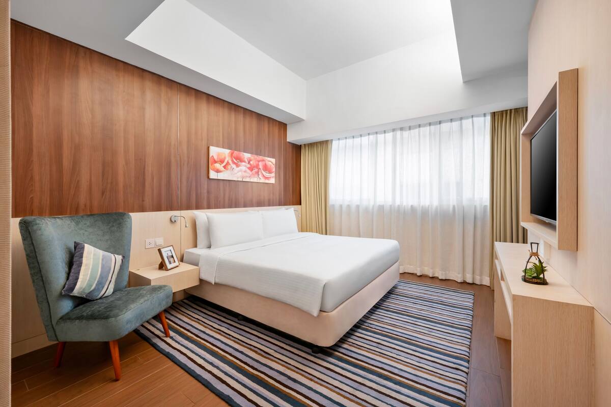 Habitació d'hotel moderna amb un llit gran, zona de seients amb una cadira, televisió de pantalla plana i una paret decorativa de fusta.