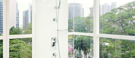 Une salle de bain moderne avec une douche à parois de verre, de grandes fenêtres et une vue sur la ville.