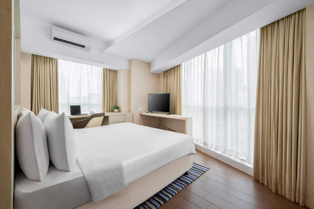 Habitació d'hotel moderna amb un llit gran, una taula de treball amb un ordinador, un televisor i vista a la ciutat.