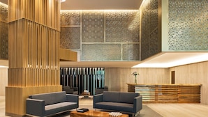 Un hall d’entrée spacieux au design moderne, comprenant un comptoir d’accueil en bois, deux canapés et une table basse.