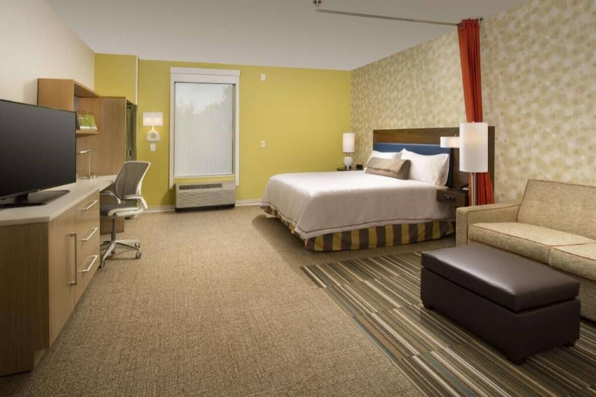 A hotel room with a bed, a sofa, a TV, a desk, and a chair.
