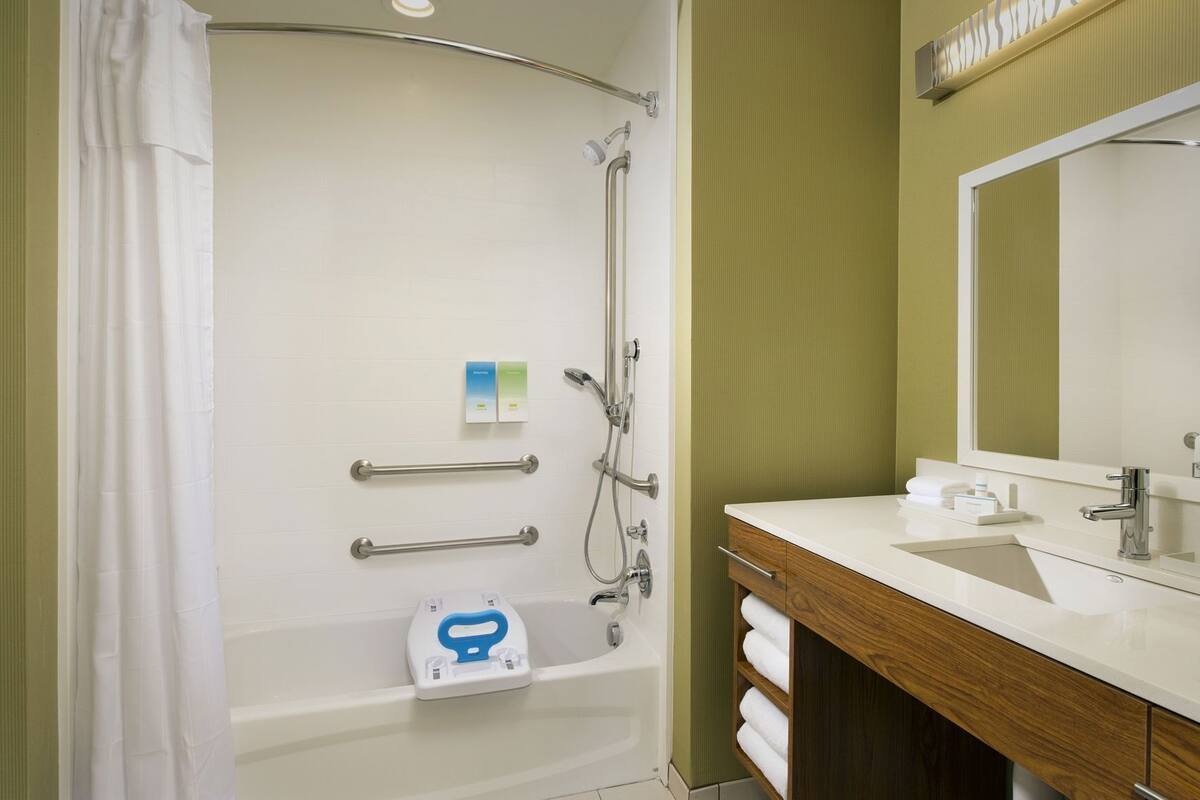 A bathroom with a shower, grab bars, a toilet, a sink, and a mirror.
