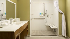 A modern bathroom with dual sinks, a shower with grab bars, and a mirror with a towel rack. - Home2 Suites by Hilton Hattiesburg (Hattiesburg)