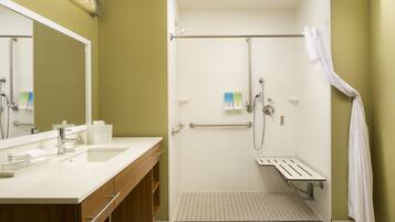 Un bagno moderno con doppio lavabo, doccia dotata di maniglie di sostegno e specchio con portasciugamani.