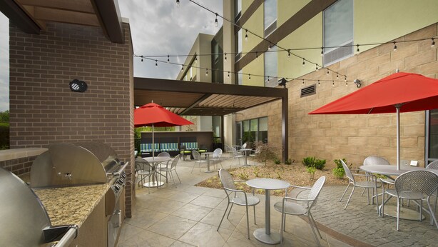 An outdoor patio with a barbecue grill, tables, and chairs, under a covered area with string lights. - Home2 Suites by Hilton Hattiesburg (Hattiesburg)