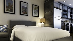 A modern bedroom with a large bed, a bedside table, and a lamp. There are framed pictures on the wall.