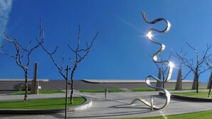 A modern sculpture in a landscaped area with a clear sky.