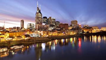 A city skyline at dusk with illuminated buildings reflecting on the water.