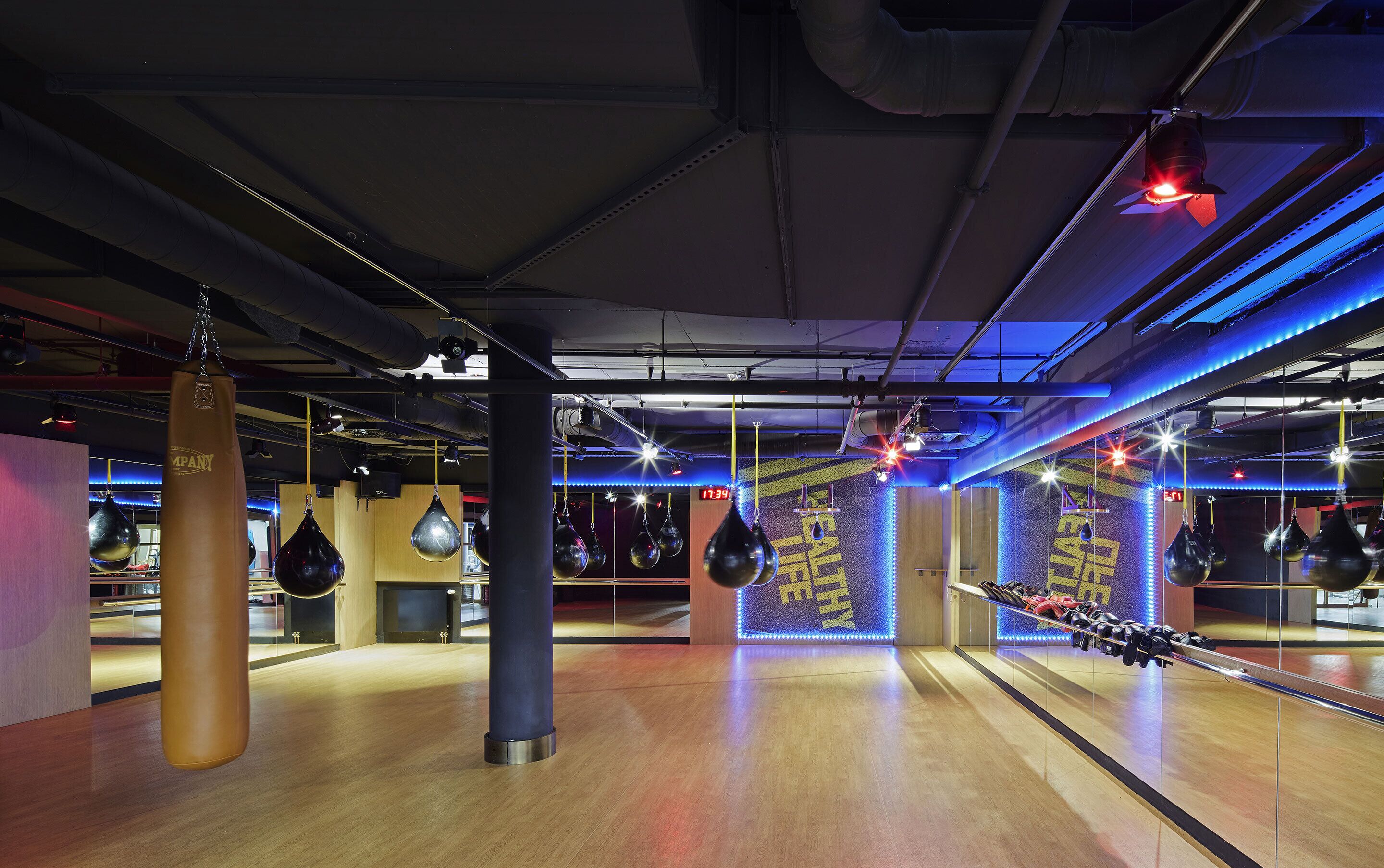Un gimnasio con suelo de madera, sacos de boxeo e iluminación LED azul.
