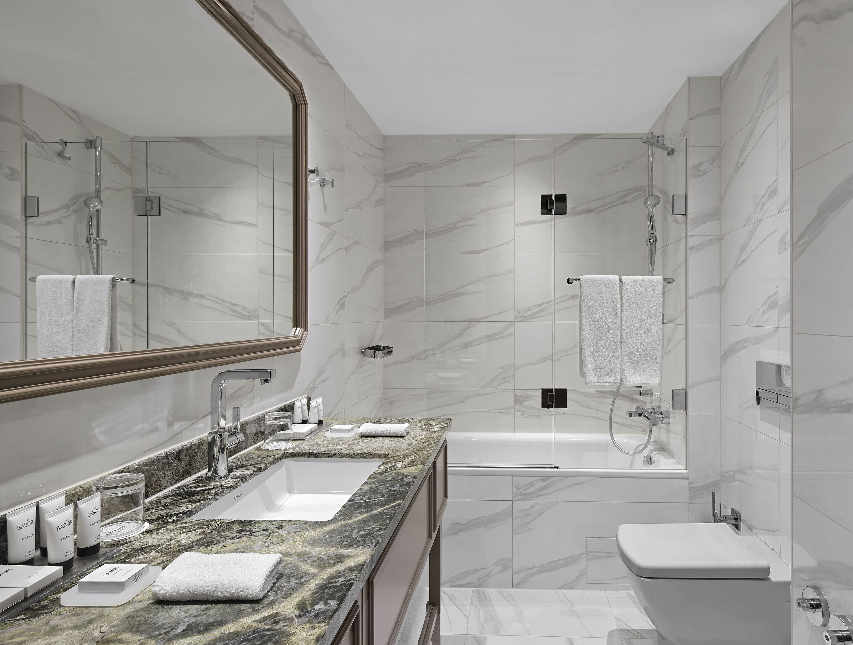 Un baño moderno con tocador de mármol, un espejo grande, una bañera y un inodoro.