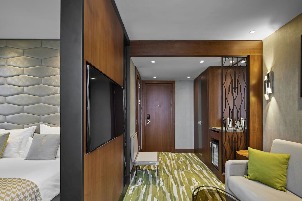 Una habitación de hotel moderna con cama, sofá, televisión y una kitchenette pequeña.