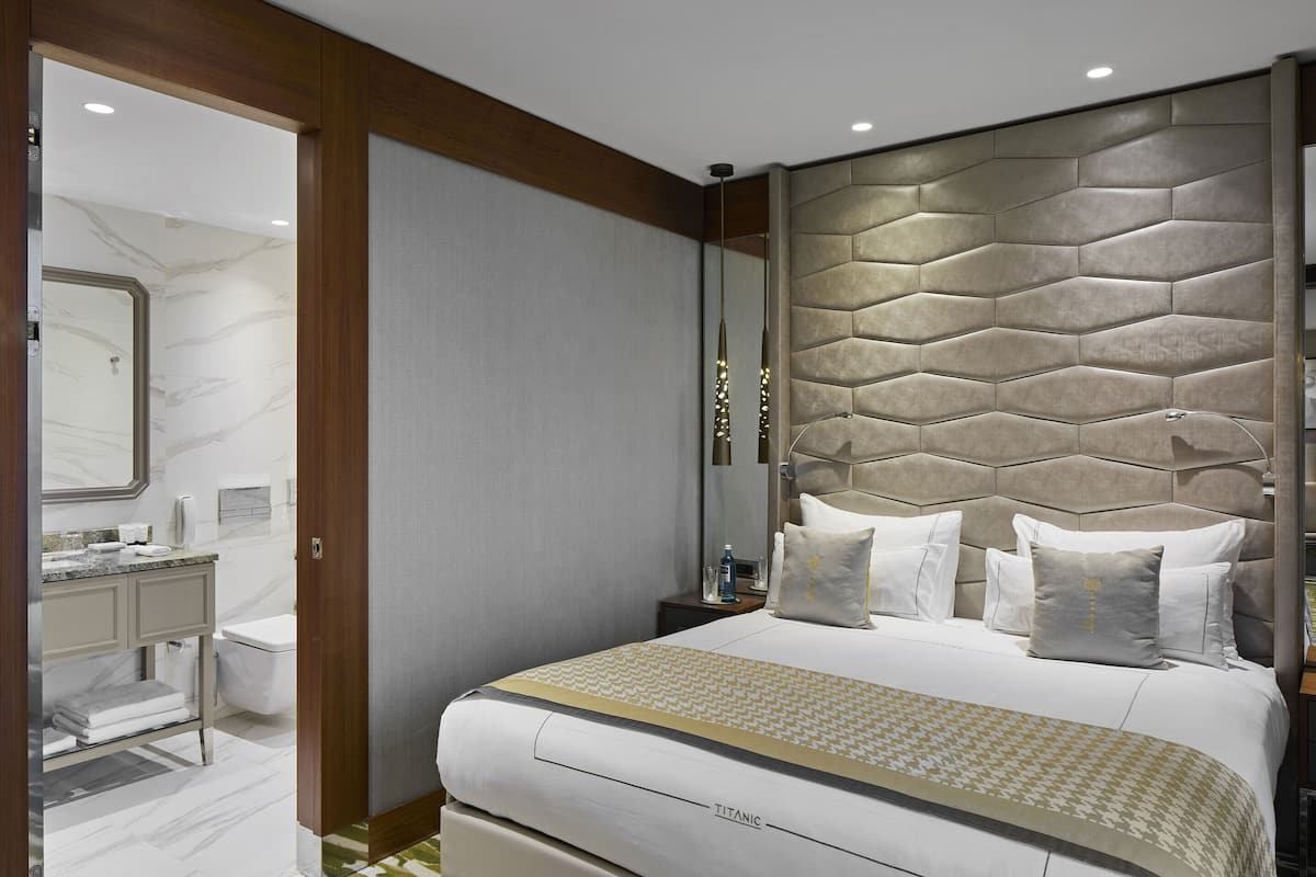 Una habitación de hotel moderna con una cama grande, cabecera con diseño geométrico, baño con pared de mármol y tocador con espejo.