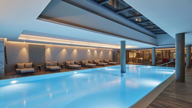Un área de piscina interior moderna con tragaluces, sillas de descanso y una recepción bien iluminada.