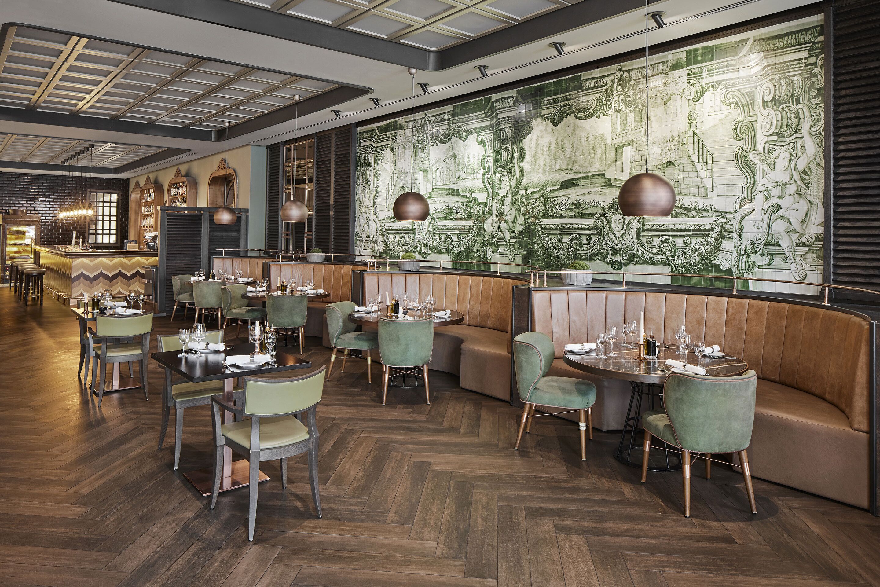 A restaurant with a herringbone wood floor, green upholstered chairs, and a large mural on the wall.