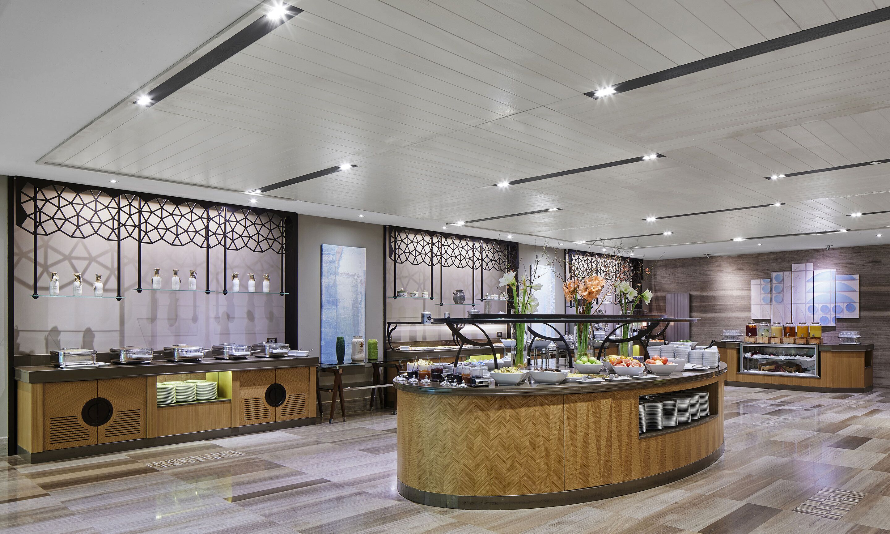 Un moderno vestíbulo de hotel con una zona de buffet central, paneles decorativos en la pared y un piso de madera pulida.