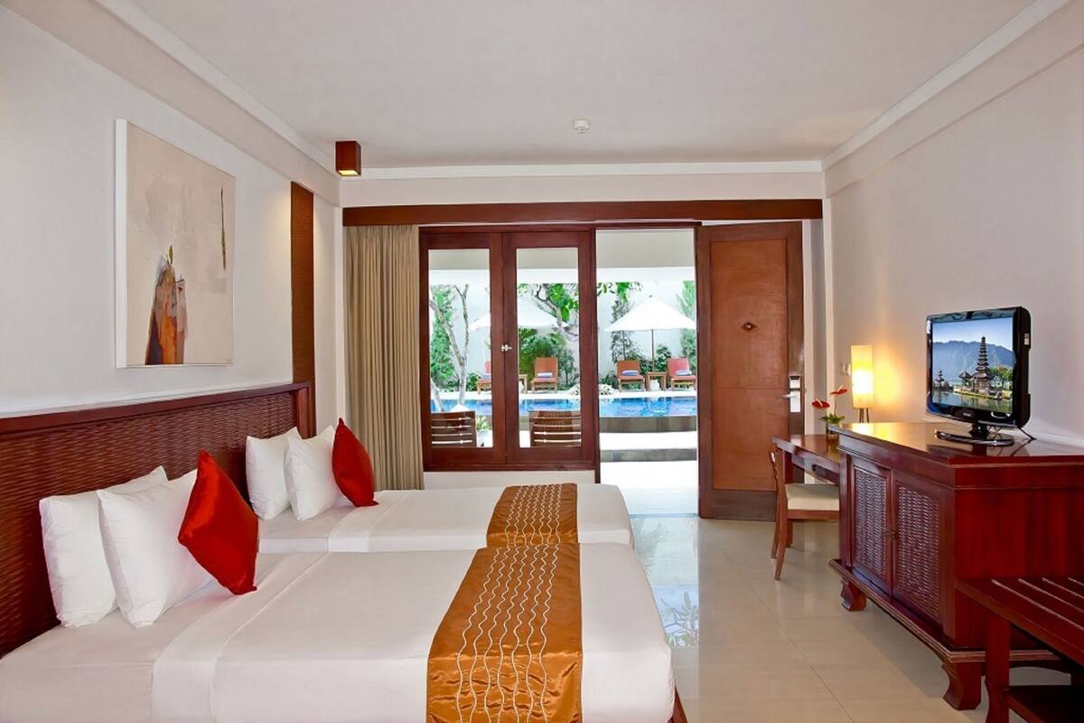 A hotel room with a bed, a desk with a TV, a view of a pool and outdoor seating.