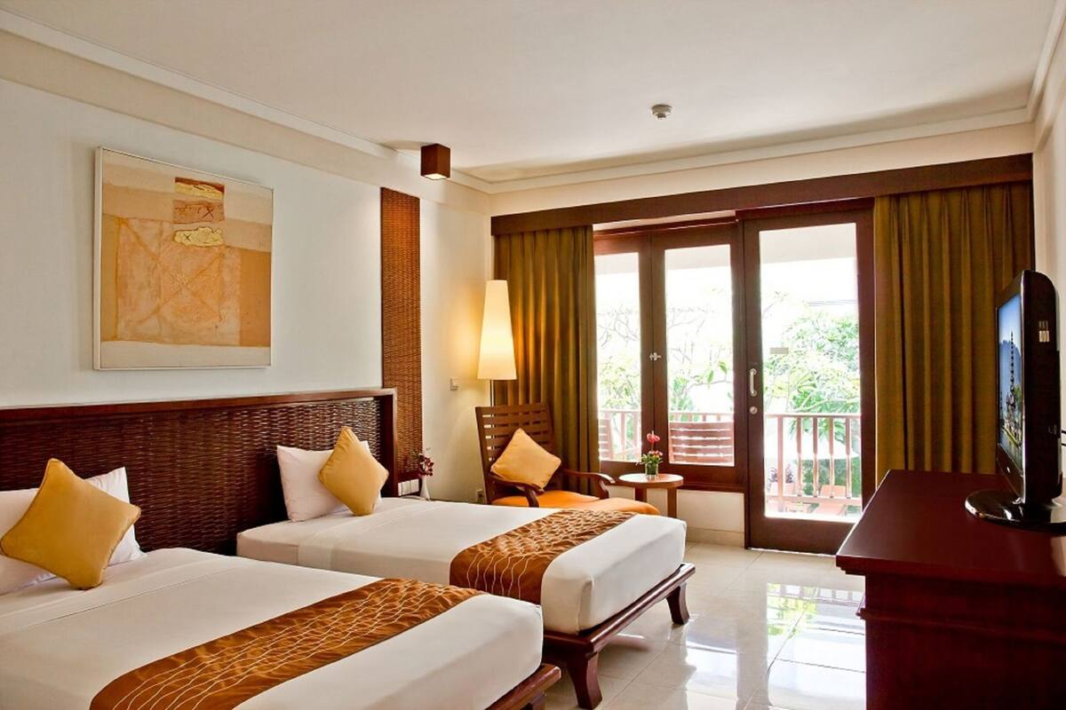 A hotel room with two beds, a TV, a balcony, and a painting on the wall.