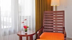 A hotel room with a wooden chair, a small round table with a vase of flowers, a lamp, and sheer curtains. - The Rani Hotel & Spa (Bali)
