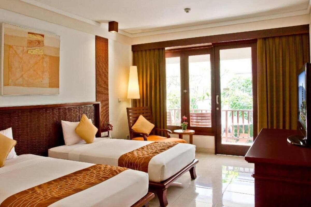 A hotel room with two beds, a television, a desk, and a balcony with curtains.