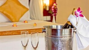 A hotel room with a bed, a bedside table with a champagne bucket and glasses, and a nightstand with a lamp. - The Rani Hotel & Spa (Bali)