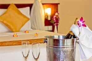 Una habitación de hotel con una cama, una mesita de noche con un cubo para champán y copas, y una mesita auxiliar con una lámpara.